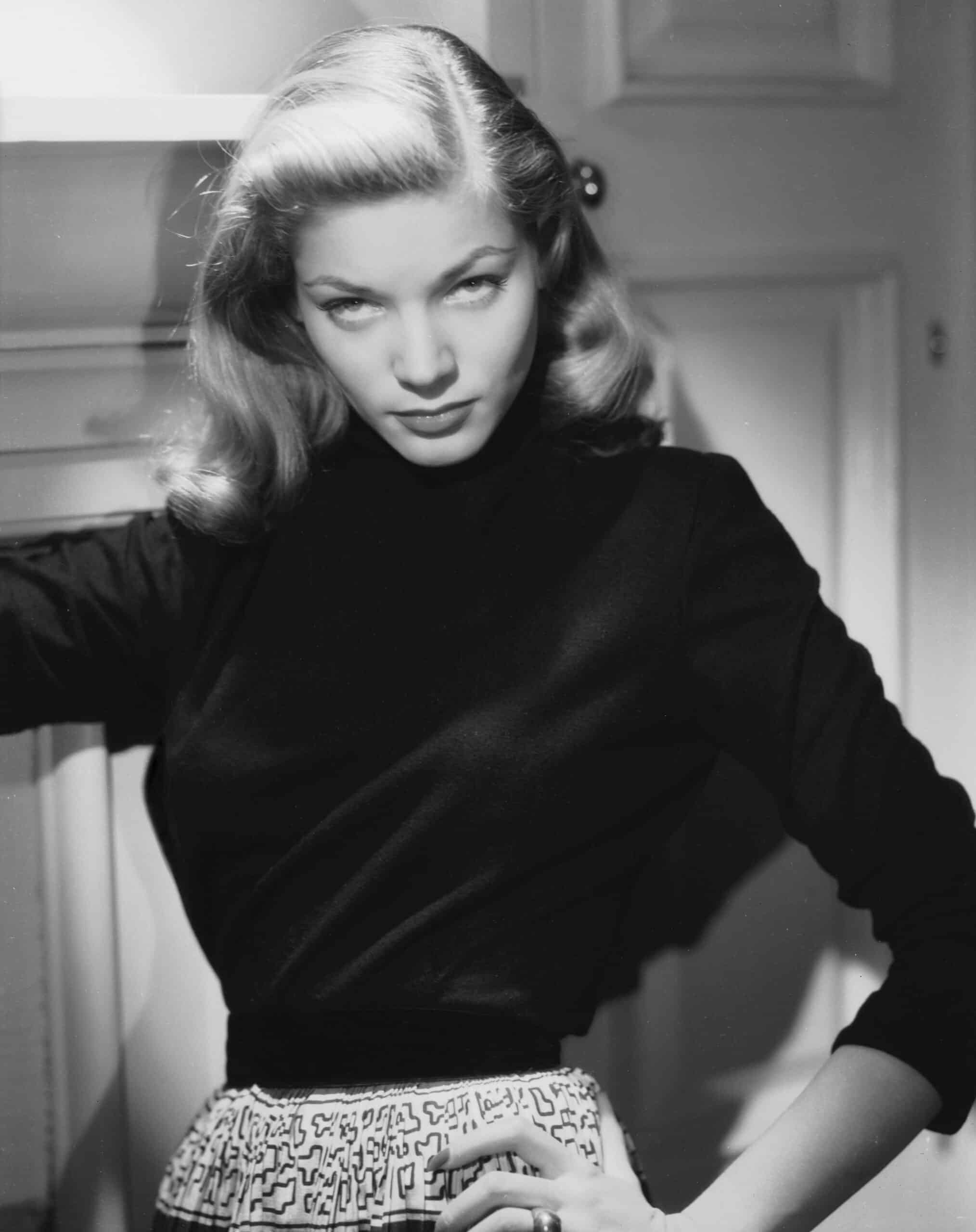 Black-and-white portrait of Lauren Bacall in a dark sweater with her hand on her hip