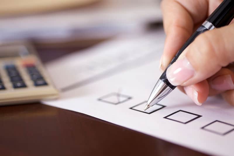 A hand marking checkboxes on a printed checklist beside a calculator.