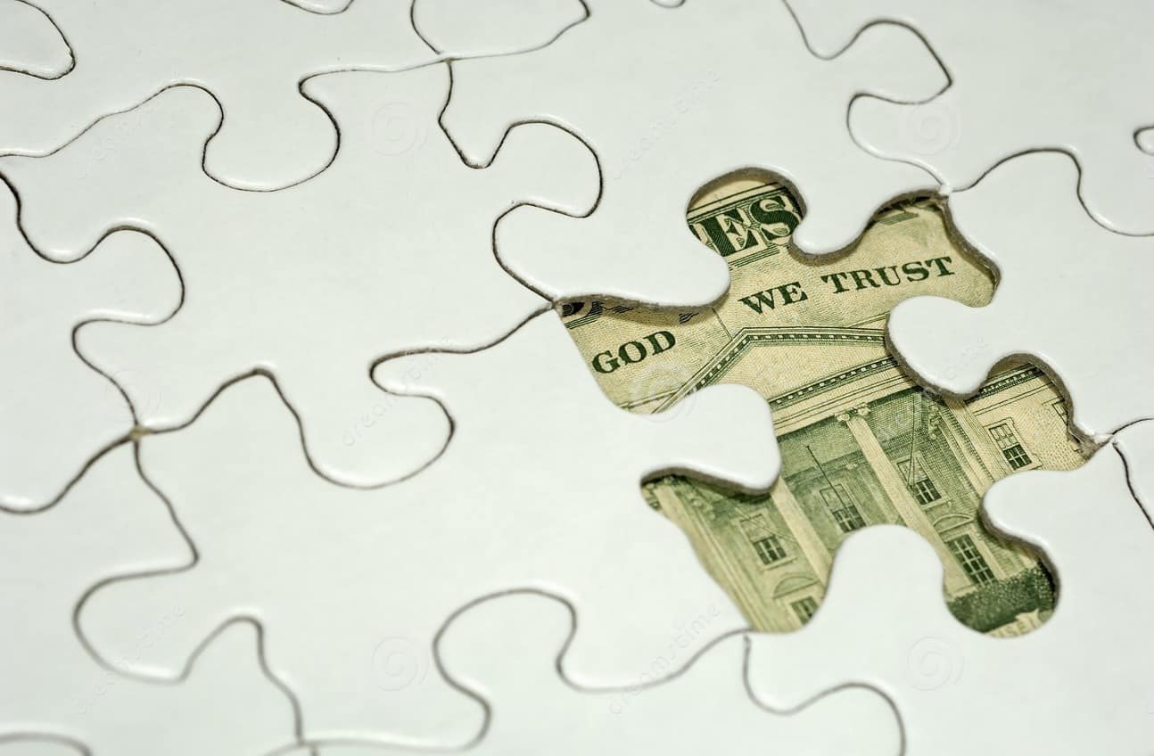 A jigsaw puzzle with a missing piece revealing "In God We Trust" from U.S. currency underneath.