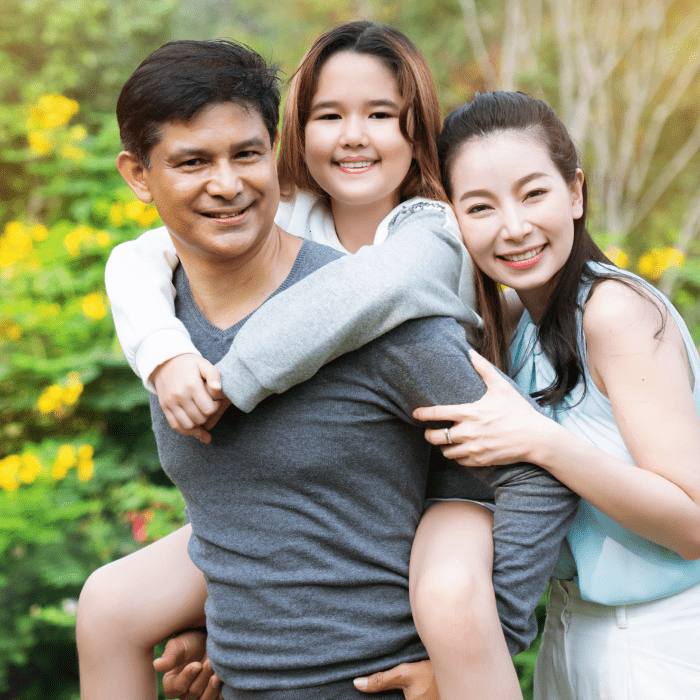 Smiling parents with their daughter riding piggyback on her father's shoulders in a garden