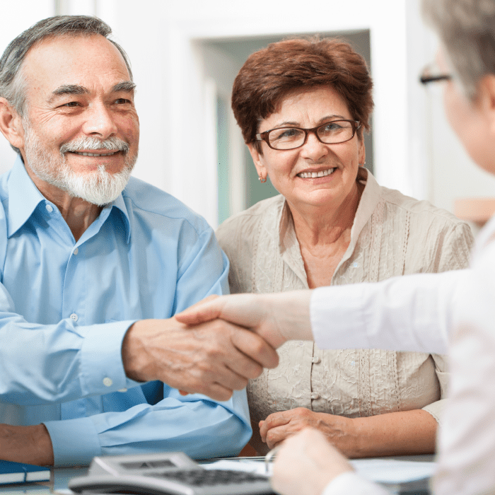 A financial adviser shaking hands with a smiling older couple across a desk.