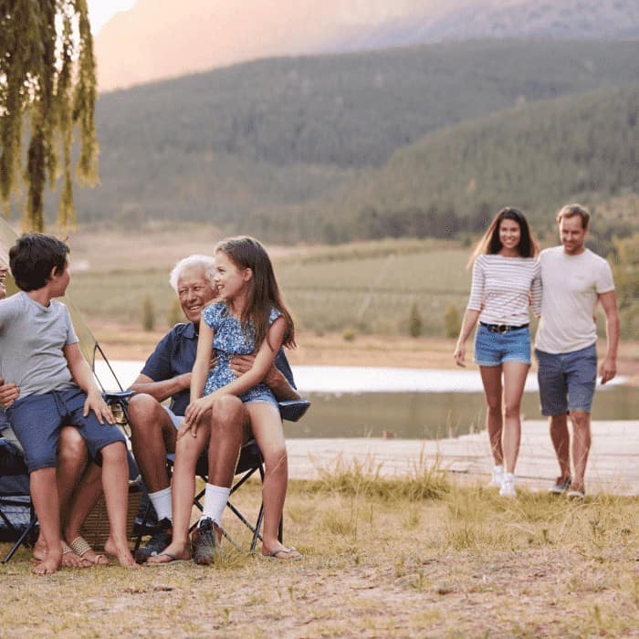 A multigenerational family laughing together outdoors at a lakeside campsite.