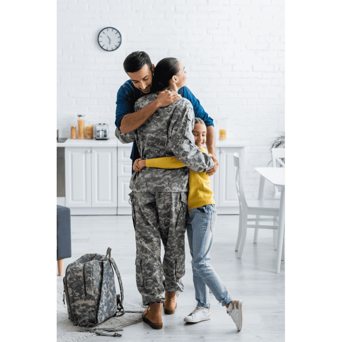 A soldier in camouflage uniform embracing a woman and young girl at home.