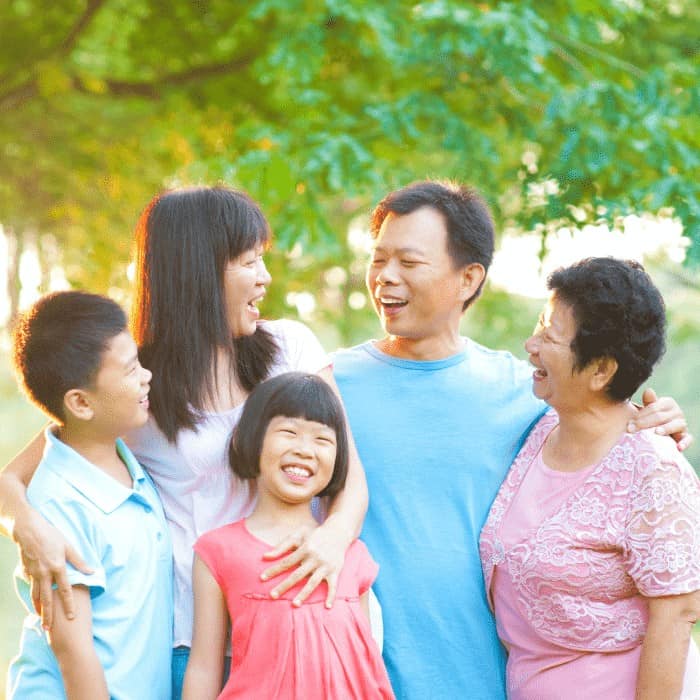 A laughing multigenerational family standing together outdoors.
