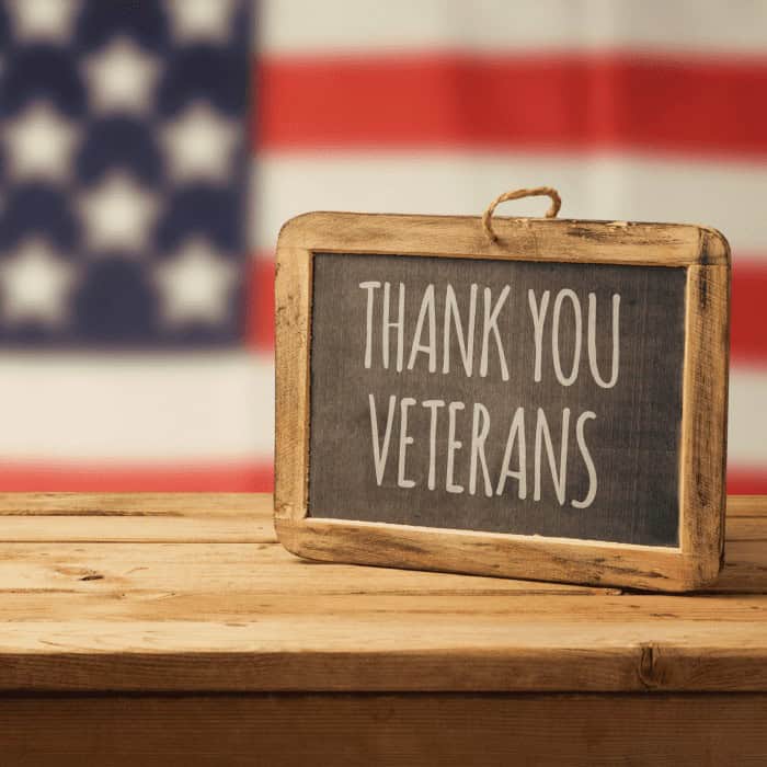 A "Thank You Veterans" chalkboard sign on a wooden table in front of an American flag.