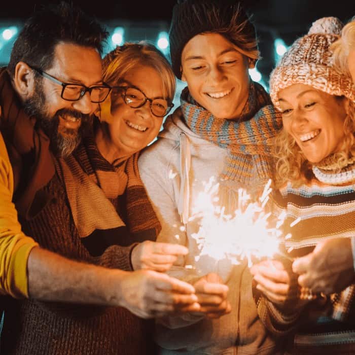 A group of friends smiling and holding sparklers at a nighttime New Year celebration.
