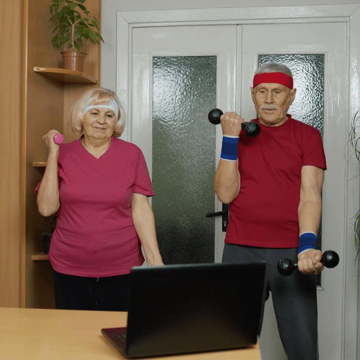 Older couple exercising with hand weights at home in front of a laptop