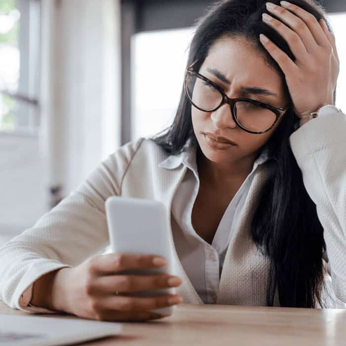 Worried woman in glasses resting her head on her hand while reading her phone