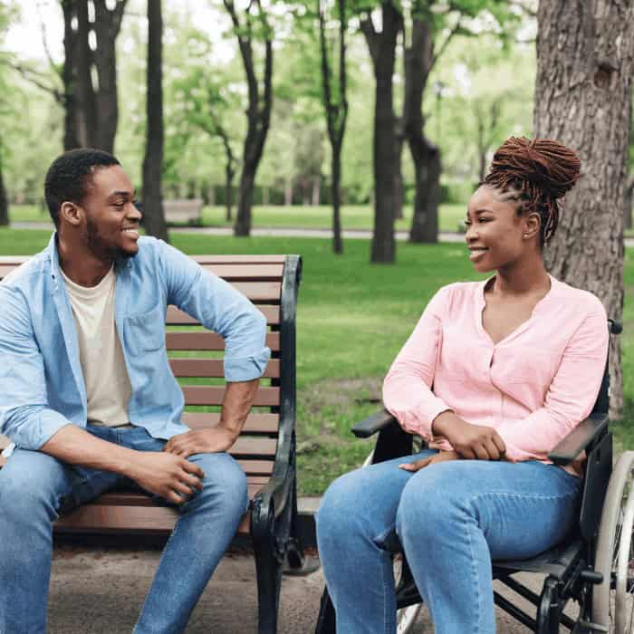 A man on a park bench talking with a woman seated in a wheelchair.