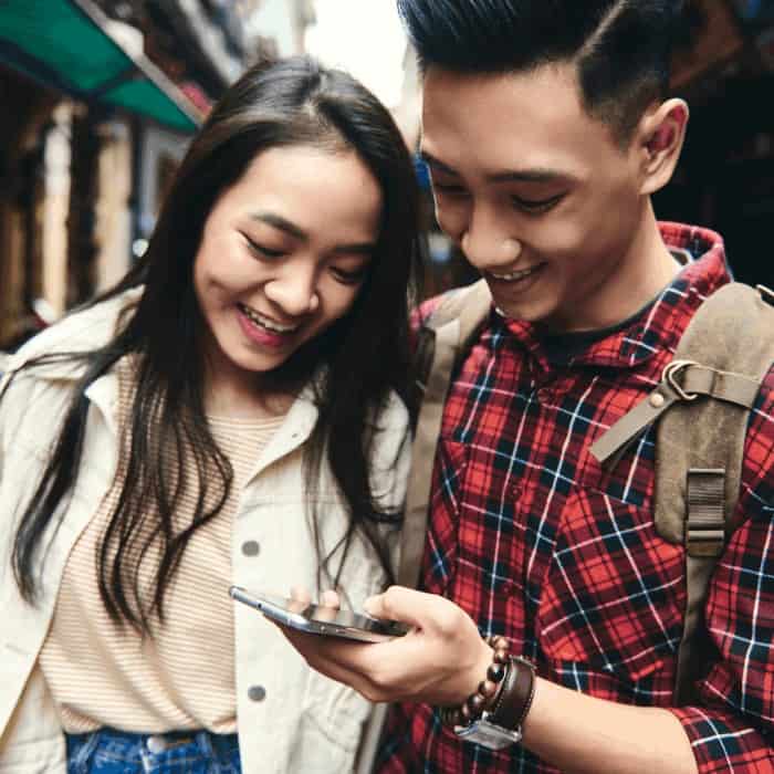 A young couple smiling at a smartphone while walking through a market street.