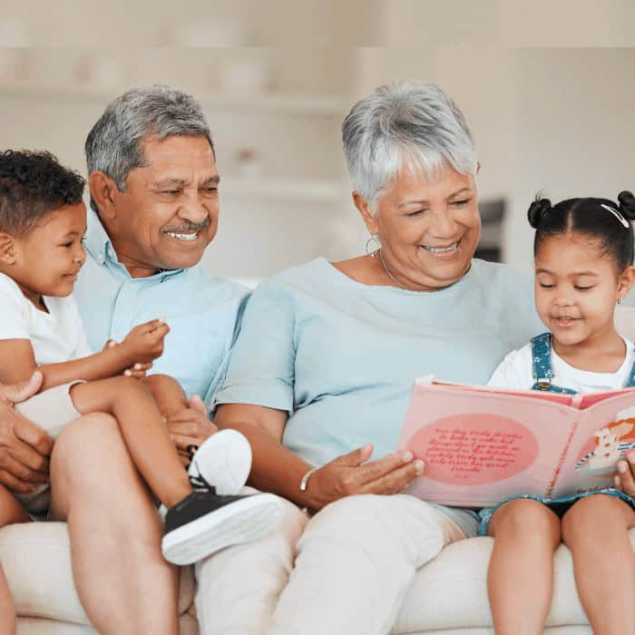 Grandparents reading a picture book with two young grandchildren on a couch.