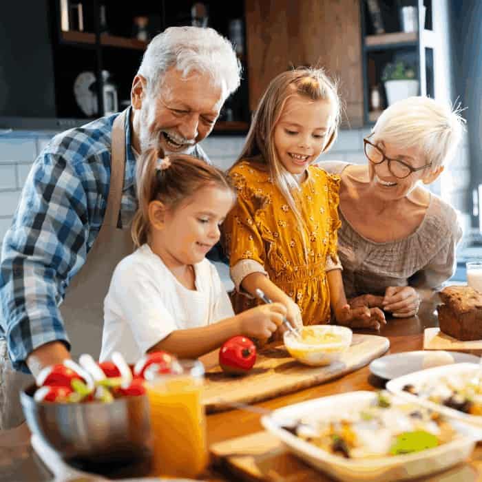 Grandparents and two grandchildren baking together in a kitchen.
