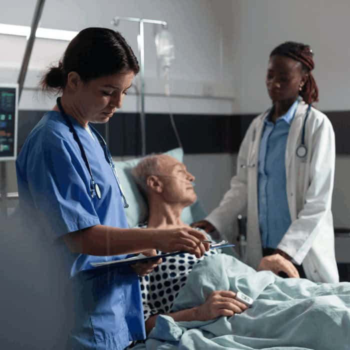 A nurse and doctor attending to an older male patient in a hospital bed.