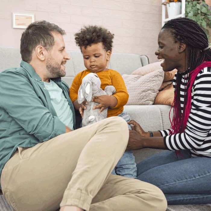 Two parents playing with a toddler and a stuffed bunny on the living-room floor.