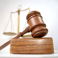 A wooden gavel resting on its block in front of a blurred set of golden scales of justice.