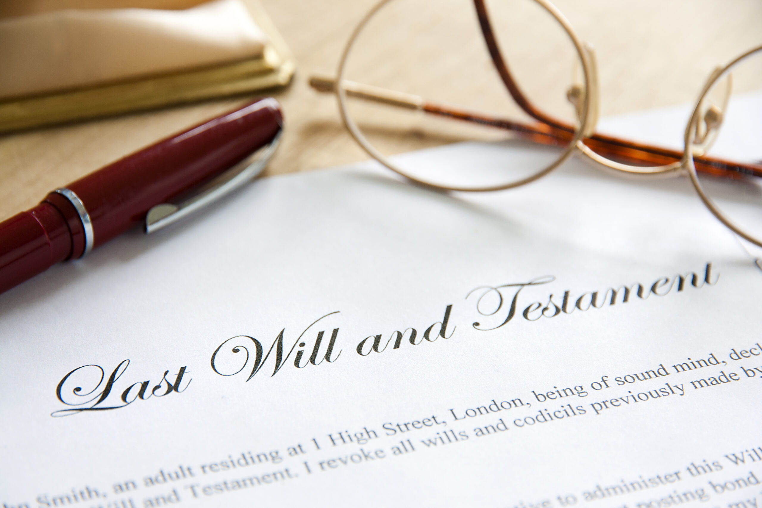 A printed Last Will and Testament document on a desk beside a red fountain pen and a pair of wire-rimmed glasses.