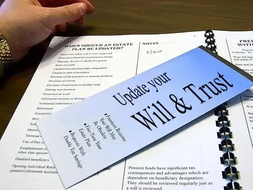 A hand rests on printed estate-planning worksheets, with a leaflet on top reading "Update your Will & Trust".
