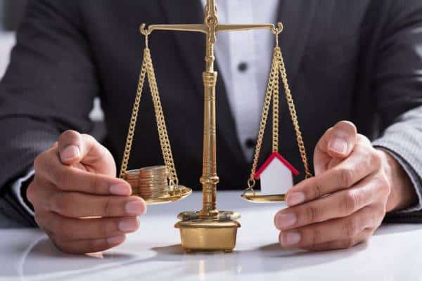 man infront of legal scale with money and house on either scale.