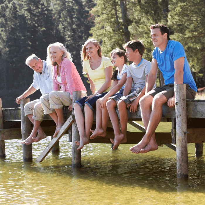Three generations of family sitting on a lake doc with their feet over the water.
