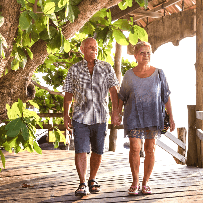 An elderly couple walking along a wooden path while holding hands, smiling.