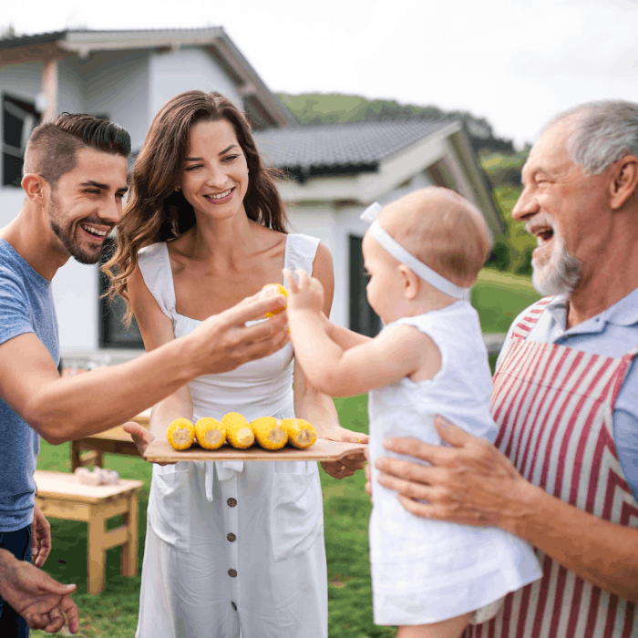 Family having a backyard bbq with grampa holding the grand child out to mom and dad.