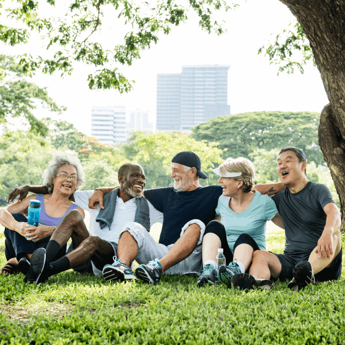 Senior friends hanging out in a park in workout clothes, smiling and laughing.